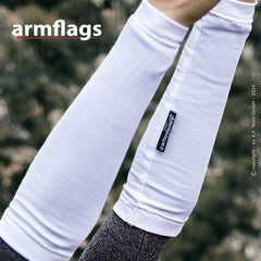 Zwei weiße Armstulpen mit schwarzem Etikett "@EichhornKreativ" auf unscharfem Hintergrund.