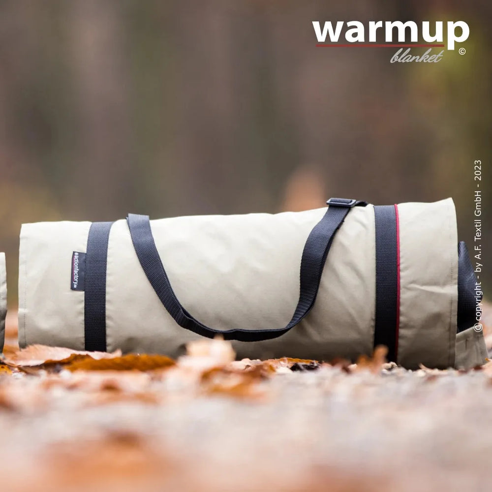 Runde, rollbare Decke in hellen Farben mit Tragriemen im Wald, umgeben von Laub. Ideal für Outdoor-Aktivitäten.