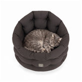 Graues, rundes Katzenbett mit weicher Polsterung, in dem eine graue Katze entspannend schläft.