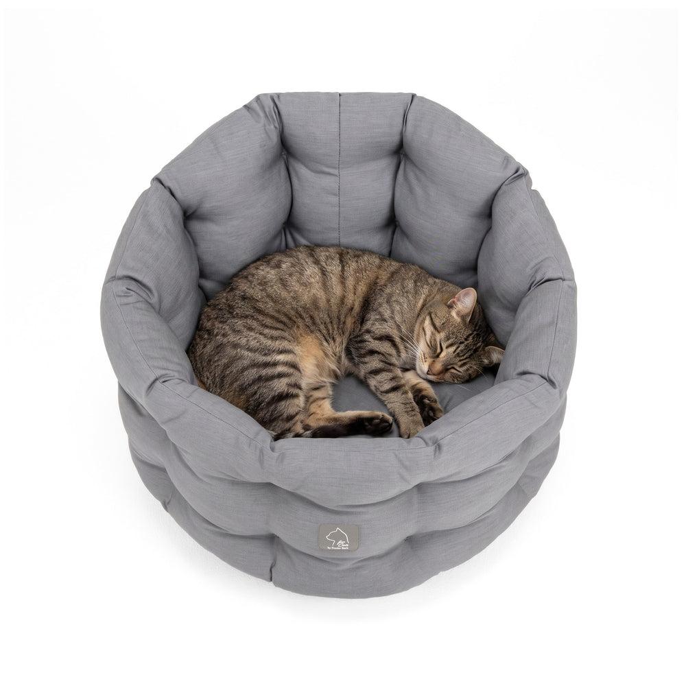 Graues rundes Katzenbett mit getigerter Katze, die entspannt darauf schläft. Weiche, gepolsterte Textur für optimale Ruhe.
