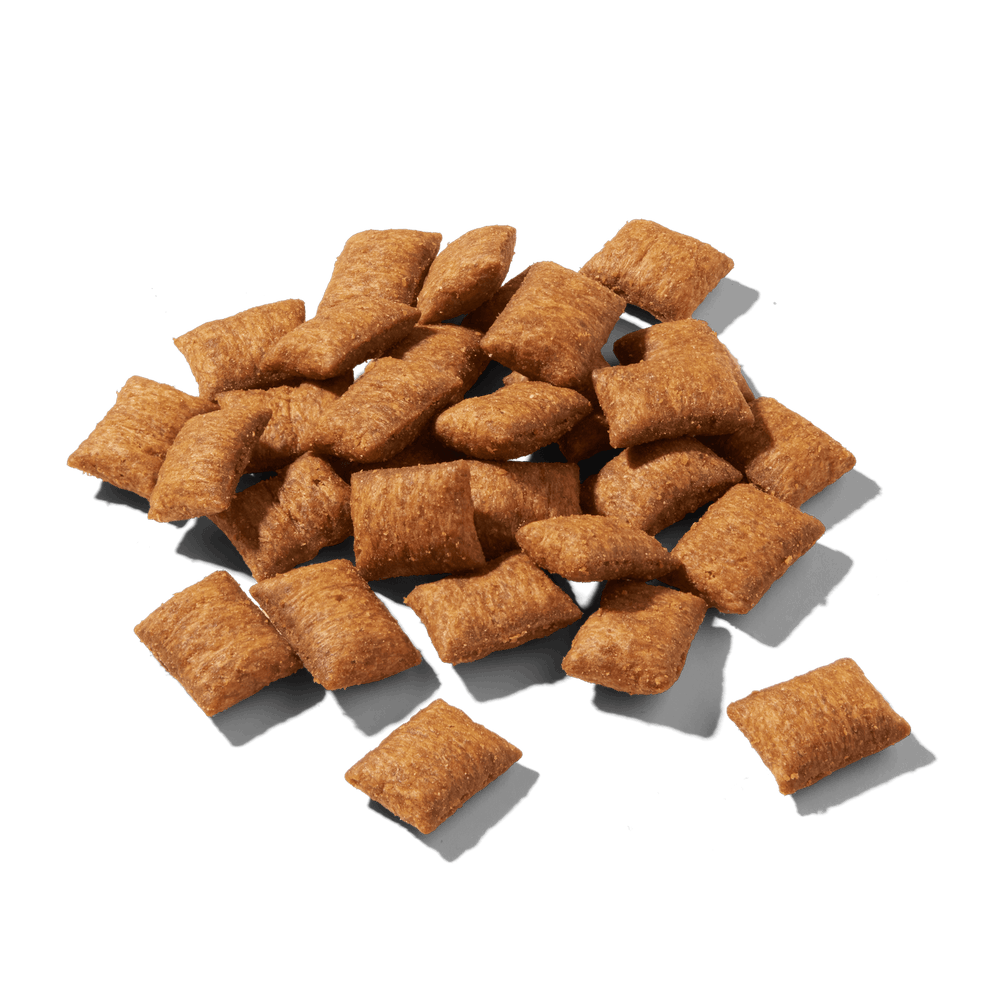 Knusprige, braune Cerealienstücke von FELIA Snacks Huhn auf schwarzem Hintergrund.