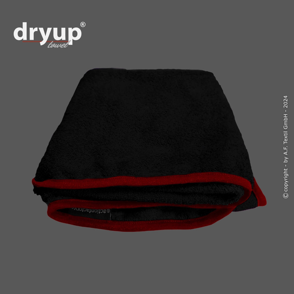 Schwarzes, gefaltetes Dryup® Handtuch mit roten Säumen auf dunklem Hintergrund. Flauschiges Material und Logo sichtbar.