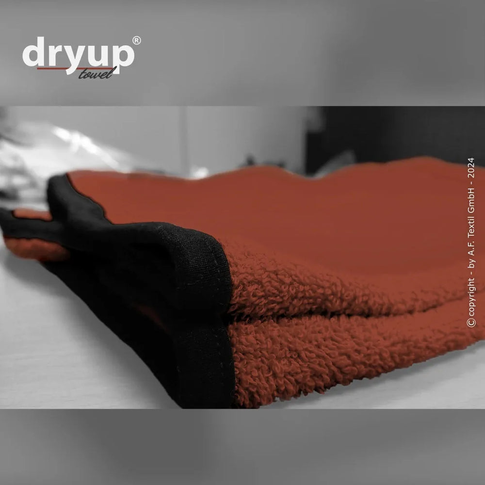 Rotes Dryup® Handtuch mit schwarzem Rand auf einer Oberfläche, flauschige Struktur und Markenlogo oben links.