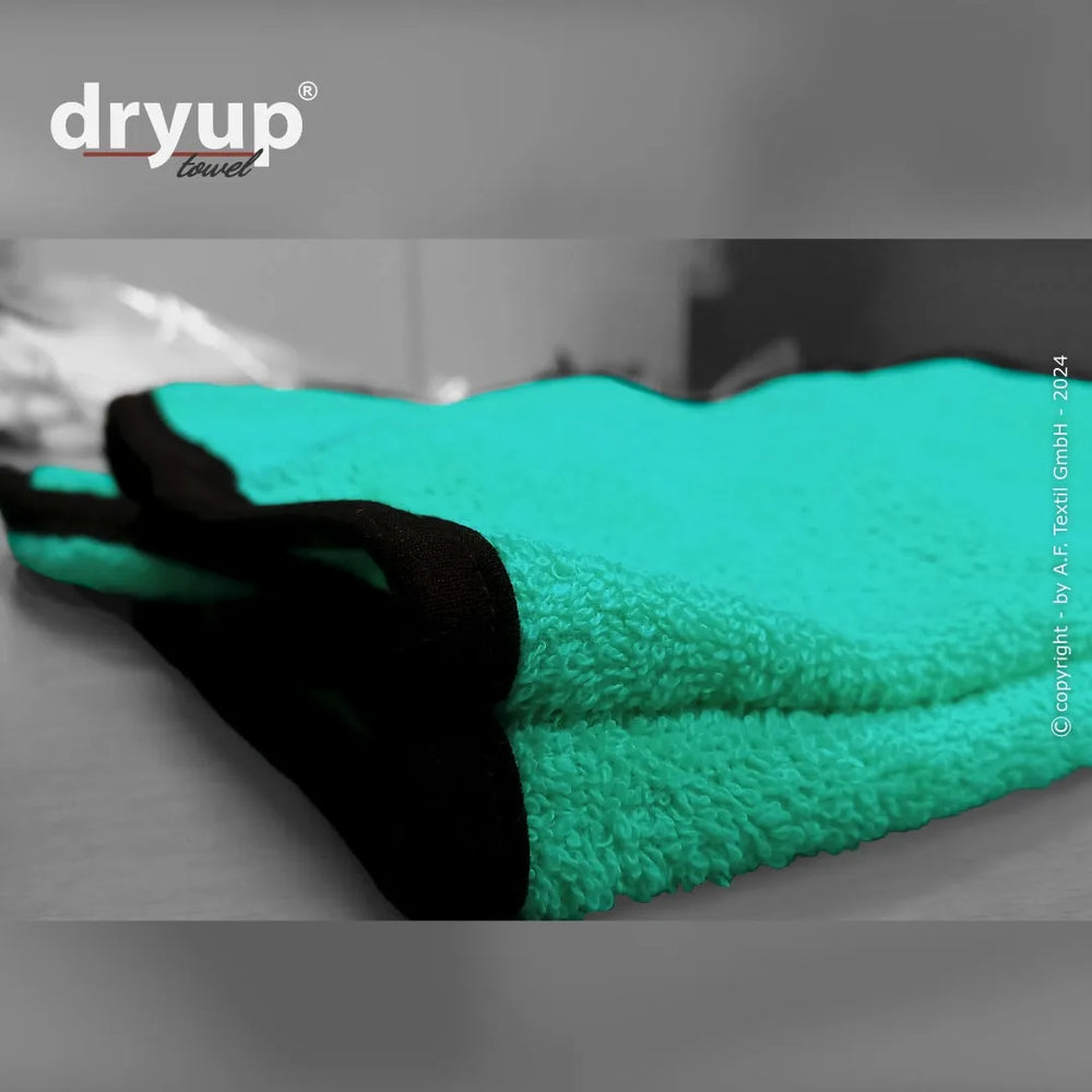 Turquoise Handtuch mit schwarzen Kanten, leicht gefaltet auf einer Oberfläche, strukturierte Textur, unscharfer Hintergrund.