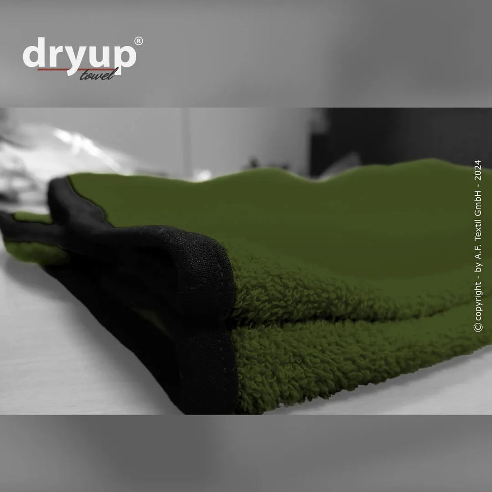 Grünes Dryup® Handtuch mit schwarzen Säumen, zusammengerollt auf einer Oberfläche, weiche Textur sichtbar.