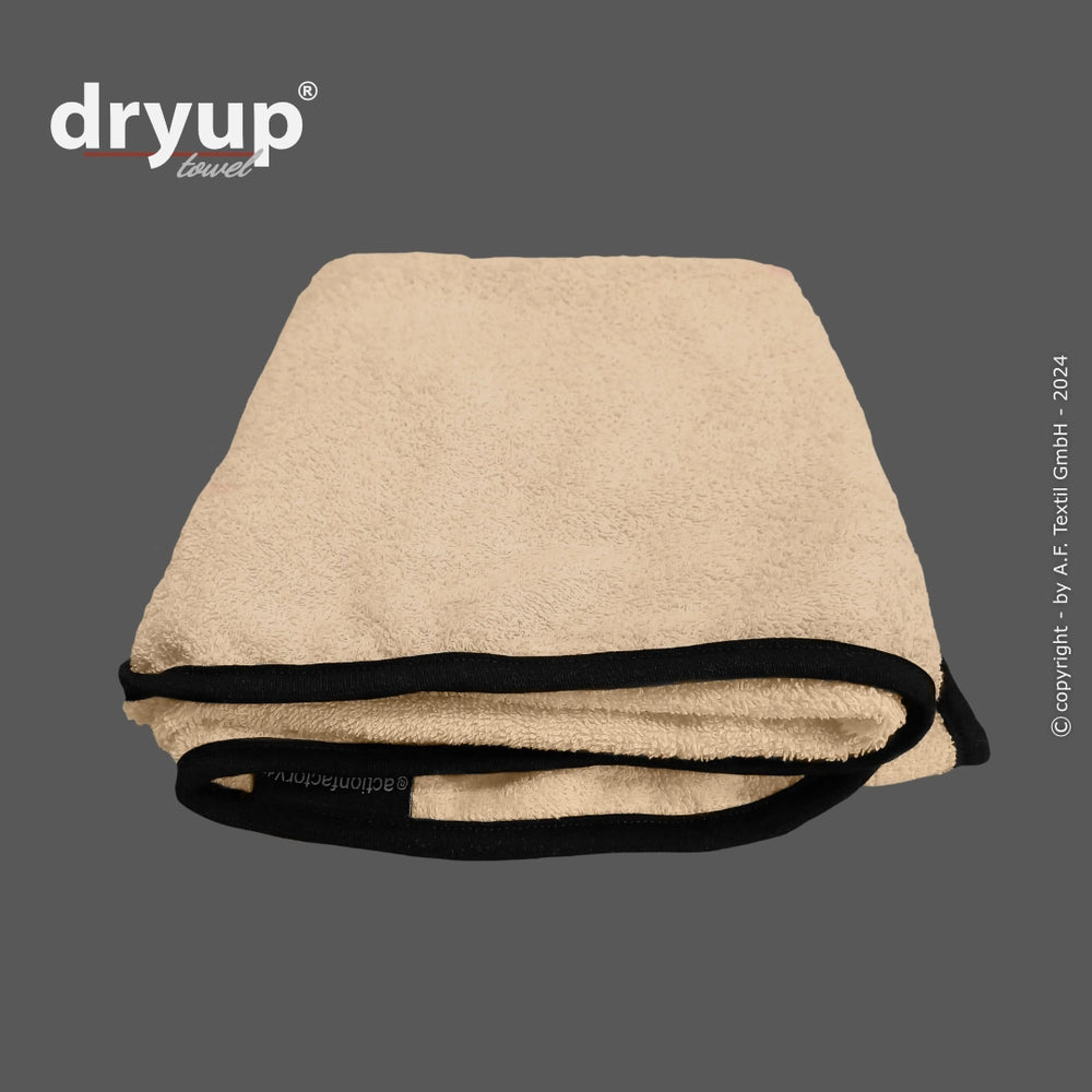 Beige gefaltetes Dryup® Handtuch mit schwarzem Rand, sichtbares Branding auf grauem Hintergrund.