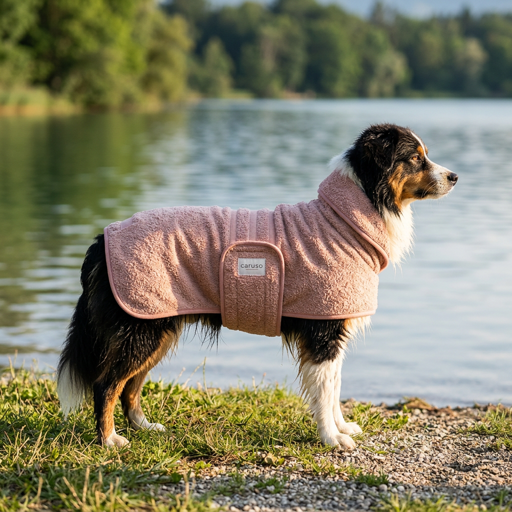 "Hund im rosafarbenen Bademantel Cozy Hug am Seeufer, umgeben von Bäumen und ruhigem Wasser."