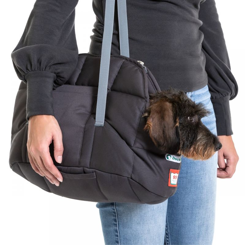 Grau wattierte Hundetasche, gehalten von einer Person, kleiner Hund schaut neugierig heraus.