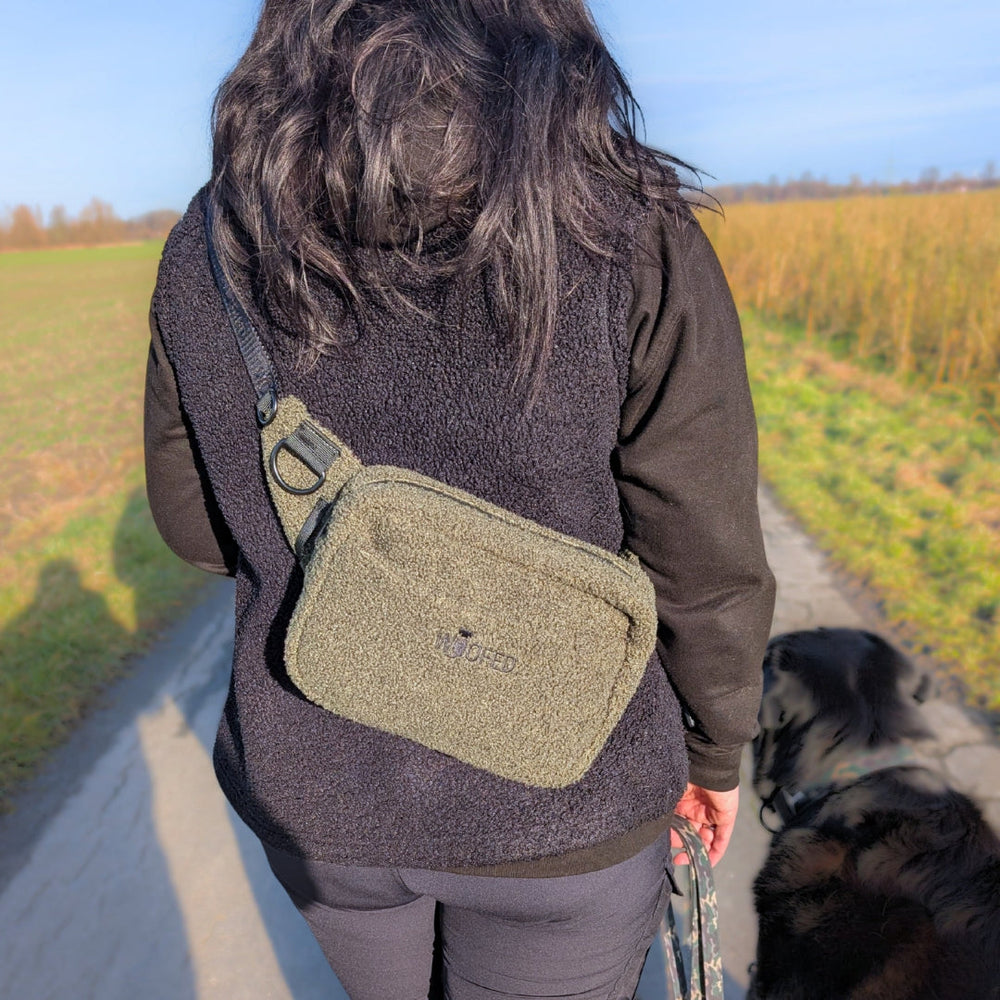 Frau mit grüner Gassitasche und schwarzem Hund, ideal als Bauchtasche oder Schultertasche für jeden Ausflug.