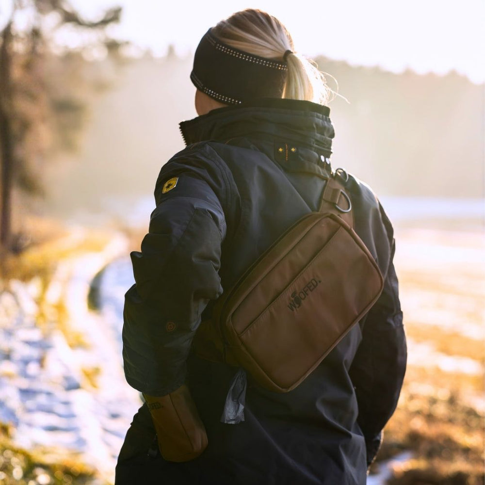 Multifunktionale Gassitasche als Bauchtasche oder Schultertasche im Winterwald mit schneebedeckten Wegen.