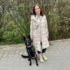 Person im beigen Wintermantel mit schwarzem Hund an WOOFLEX® Classic Umhängeleine auf Gehweg.
