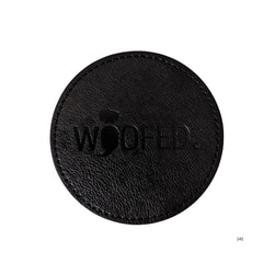 Runder, schwarzer Leder-Getränkeuntersetzer mit eingeprägtem "WOOFED." Schriftzug, schlichtes und elegantes Design.