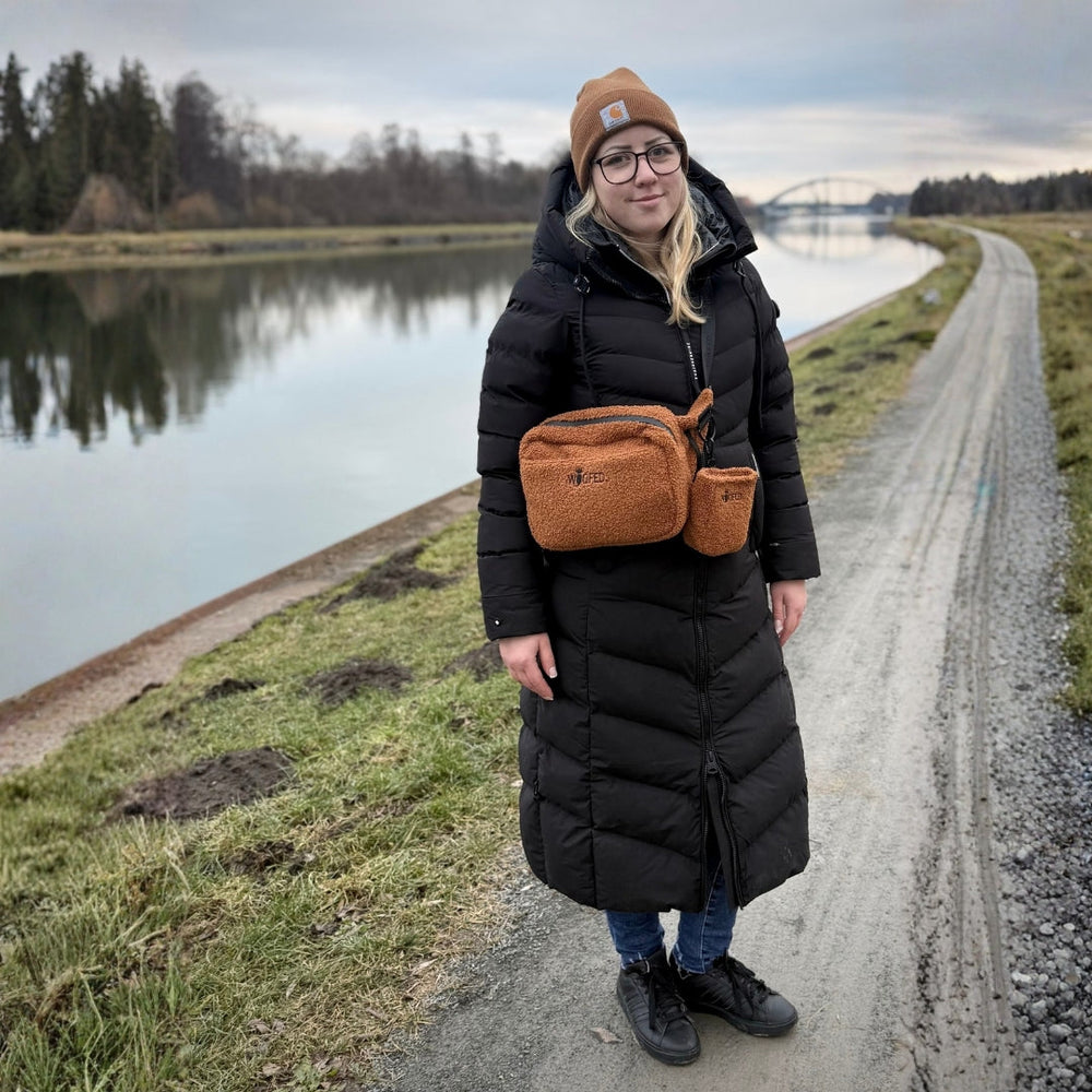 Person am Ufer trägt einen schwarzen Wintermantel und eine multifunktionale braune Gassitasche als Bauchtasche.