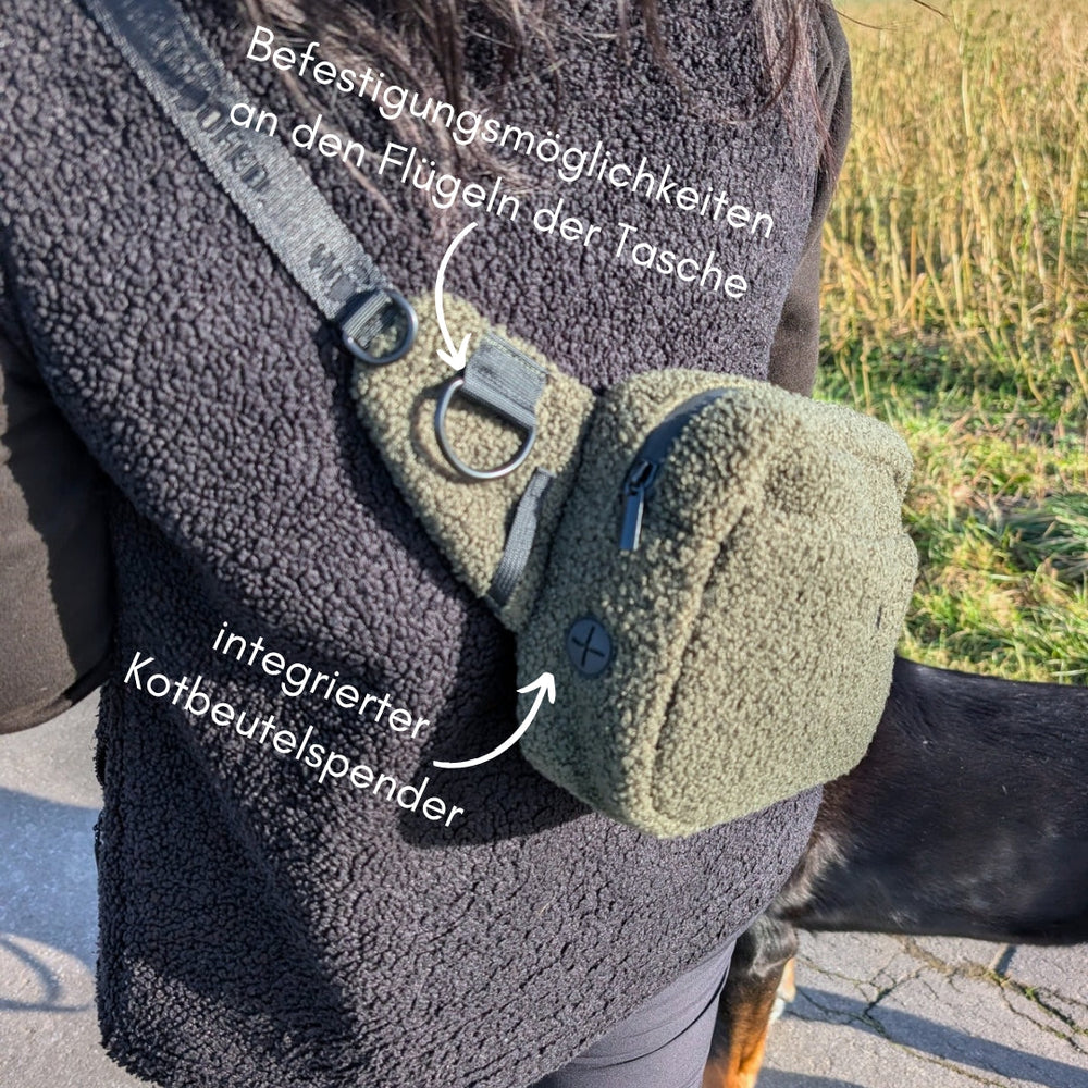 "Hundebesitzer mit olivgrüner Multifunktionstasche im Freien, ausgestattet mit Kotbeutelspender und Befestigungsmöglichkeiten."