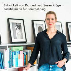Frau mit blonden Haaren in modernem Raum, schwarzes Hemd, umgeben von Tierbildern und Bücherregalen.