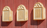 Drei dekorative Reibegeräte aus Keramik an roter Wand, ovalformin mit kleinen Löchern für Wildbienen.