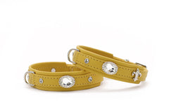 Zwei gelbe Lederhundehalsbänder mit silbernen Beschlägen und funkelnden Steinen, eines mit elegantem Emblem.
