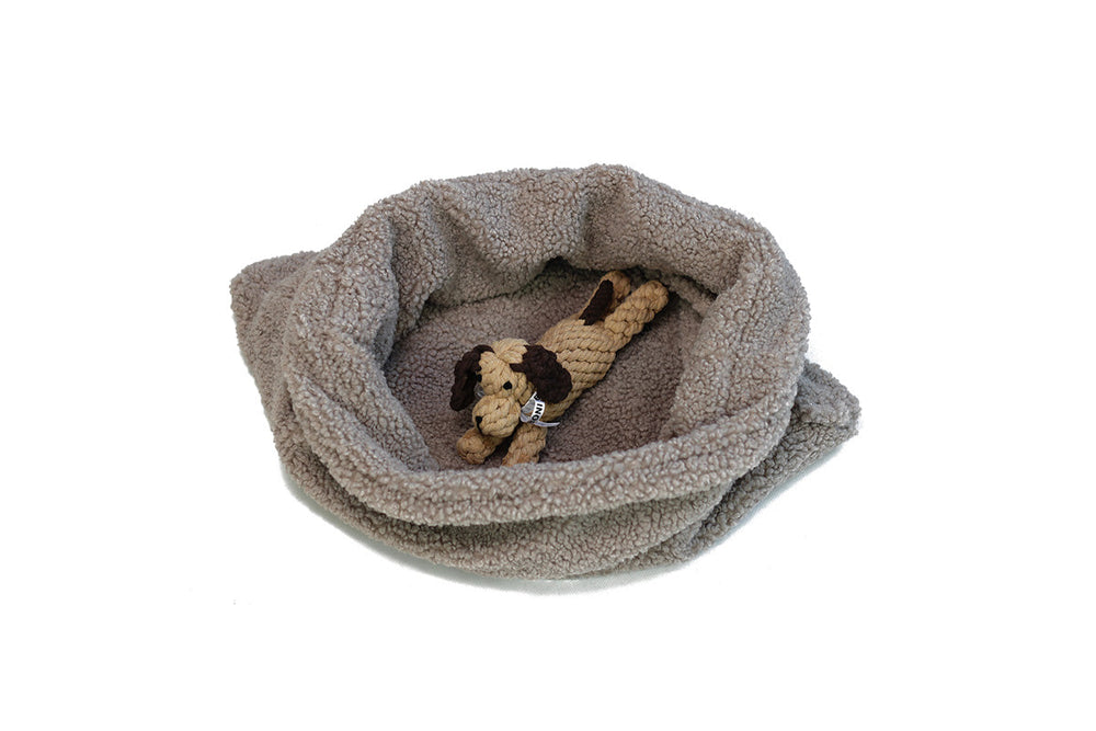 "Beiges Hunde-Schlafsack mit erhöhtem Rand und Kauspielzeug in Hundeform aus Seil."