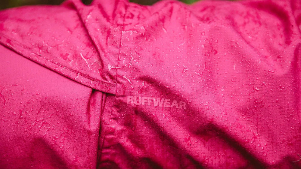 Wasserabweisender pinker Regenmantel für Hunde mit RUFFWEAR-Logo und sichtbar abperlendem Wasser.