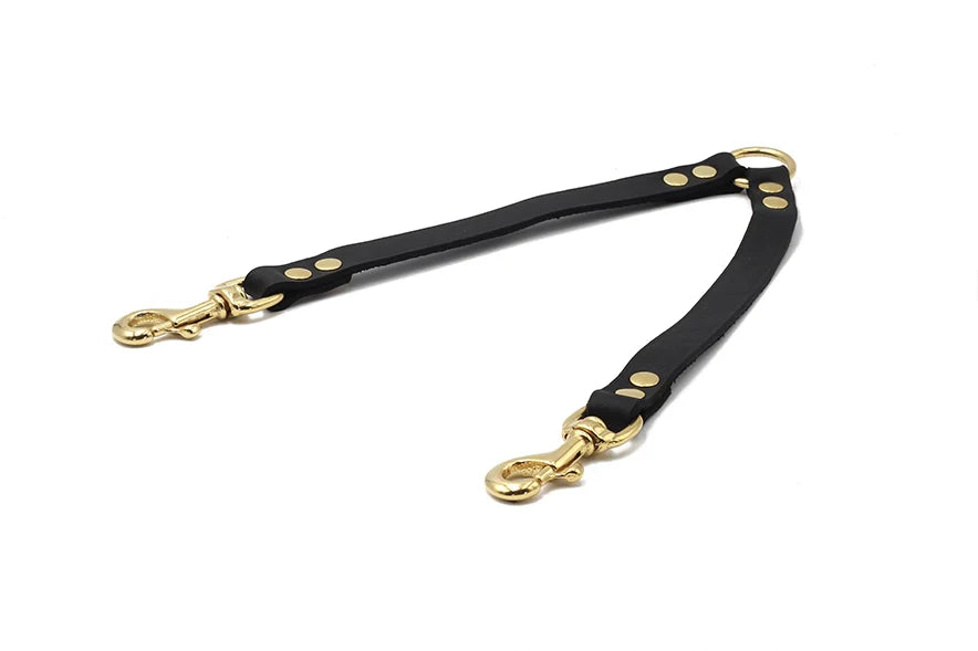 Schwarzer Lederhalsbandverbinder für zwei Hunde mit goldfarbenen Haltestellen und Karabinerhaken.