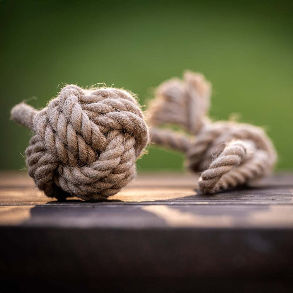 "Straff gebundener Knoten aus Hanfseil, daneben ein weiteres Seilstück auf unscharfem, sanft grünem Hintergrund."