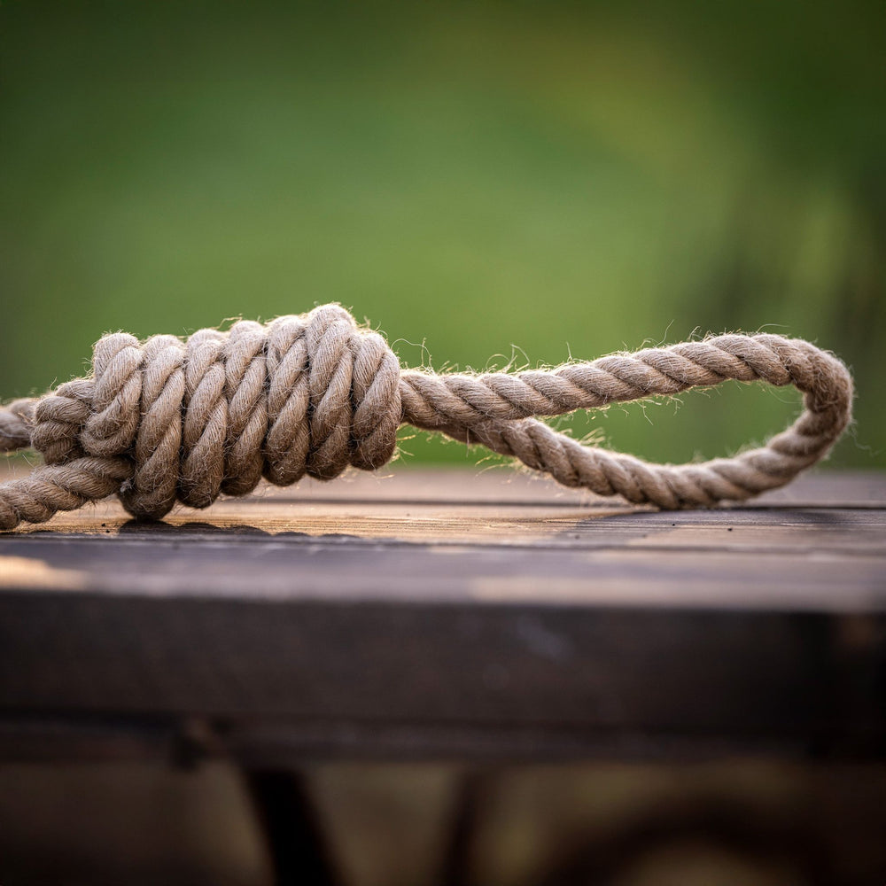 Dicht gewickelter Knoten aus Hanfseil auf Holz, umgeben von unscharfem grünem Gras – ideal für die Zahnpflege von Haustieren.
