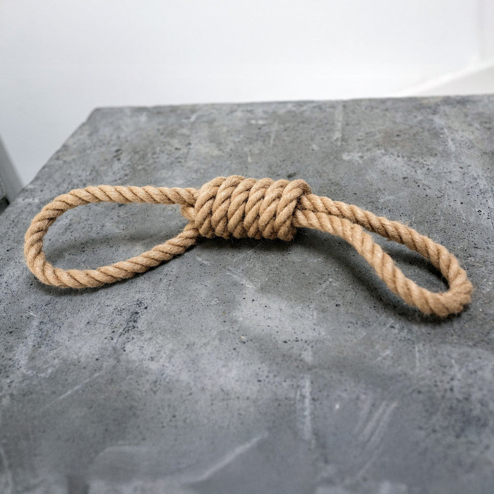 Zahnpflegender Hanfseil-Zergel in Schlaufform auf grauer Oberfläche, ideal fürs Spielen mit Hunden.