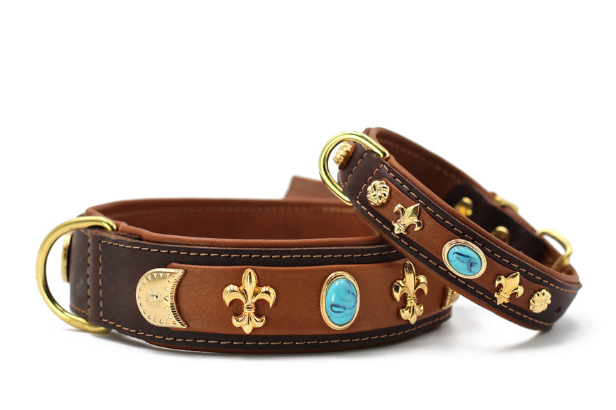 Braune Lederhundehalsbänder mit goldenen Verzierungen und blauen Steinen, eines breiter, das andere schmaler.