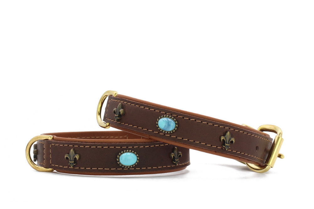 "Zwei elegante braune Lederhundehalsbänder mit goldfarbenen Beschlägen und blauen Steinelementen, verziert mit Lilienmotiv."