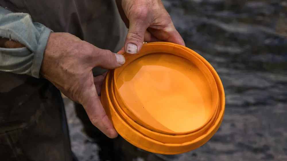 Faltbarer Hundenapf in den Händen einer Person am Wasser, ideal für Outdoor-Abenteuer mit Haustieren.