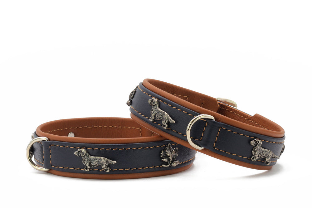 Zwei dunkelblaue Lederschnüffelhalsbänder mit brauner Innenseite und silbernen Hundemotiven und Eicheln.