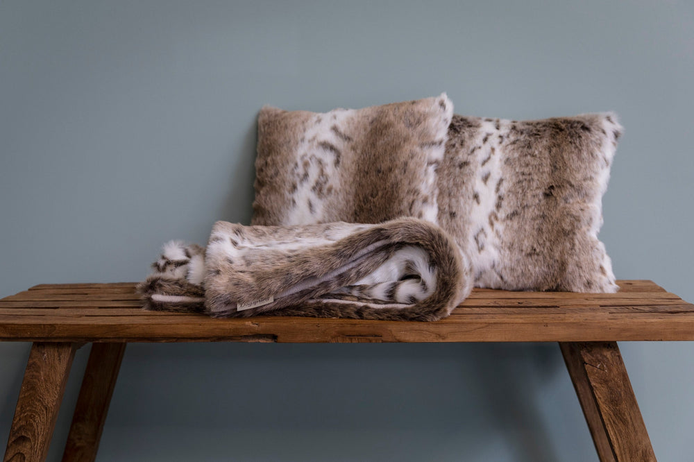 Dekorative Kissenbezüge aus Webpelz in Brauntönen auf einer Holzbank mit gefaltetem Fell.