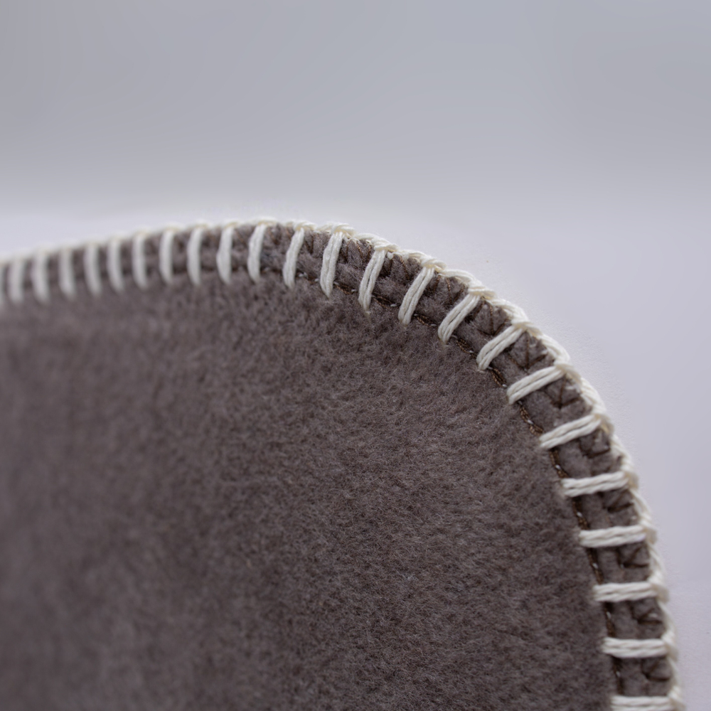 Nahtdetail einer runden grauen Filzdecke mit hellem Faden, das die hochwertige Verarbeitung und Textur zeigt.