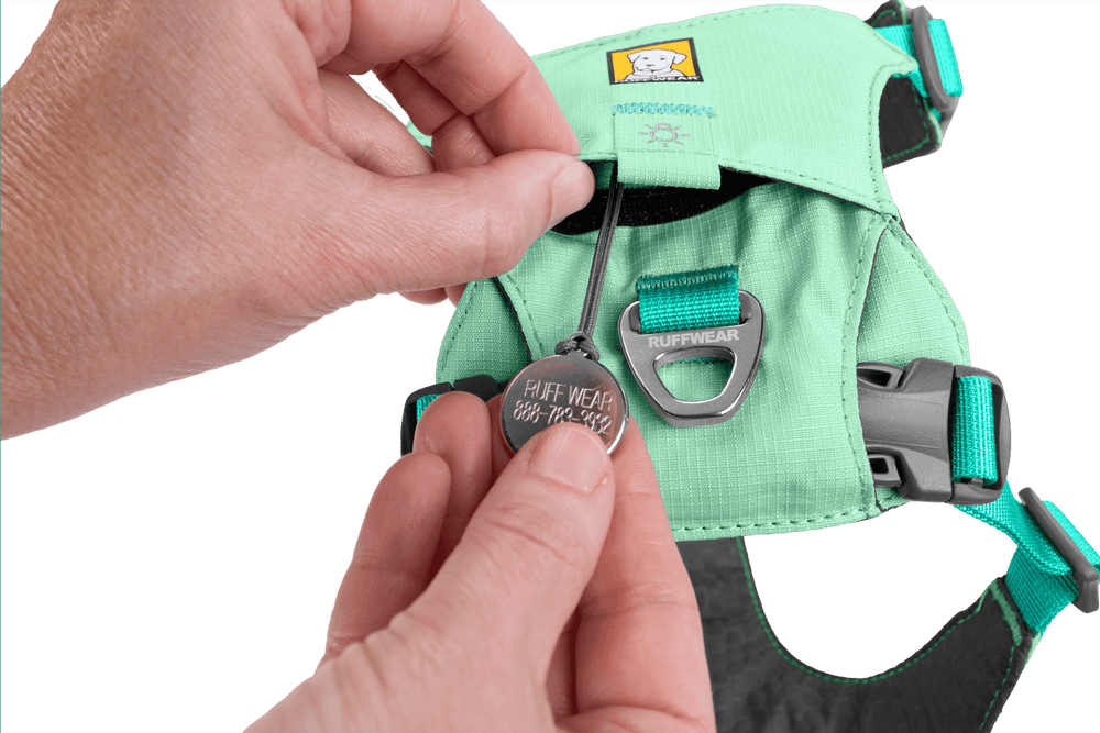 „Metallanhänger mit ‚RUFFWEAR‘ an grünem Hi Light™ Hundegeschirr mit Schnalle und reflektierenden Elementen.“