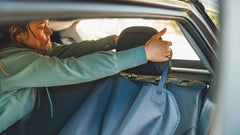 Person im Auto mit Dirtbag™ Autositzbezug für Hunde, Tasche über der Kopfstütze, grauer Kapuzenpullover.