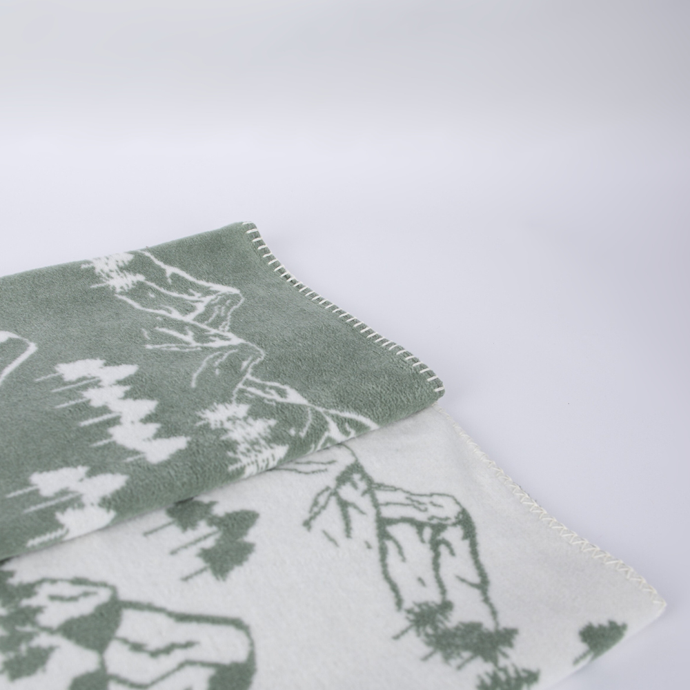Zweifarbige Decke Caruso Forrest mit Berglandschaft in Grün und weißen Motiven. Ideal für gemütliche Abende.