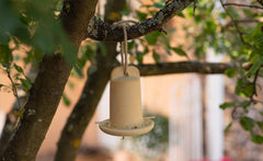 Hängender Vogelfutterspender aus hellem Material, sicher befestigt an einem Baumast. Ideal für Ihr Gartenornament.
