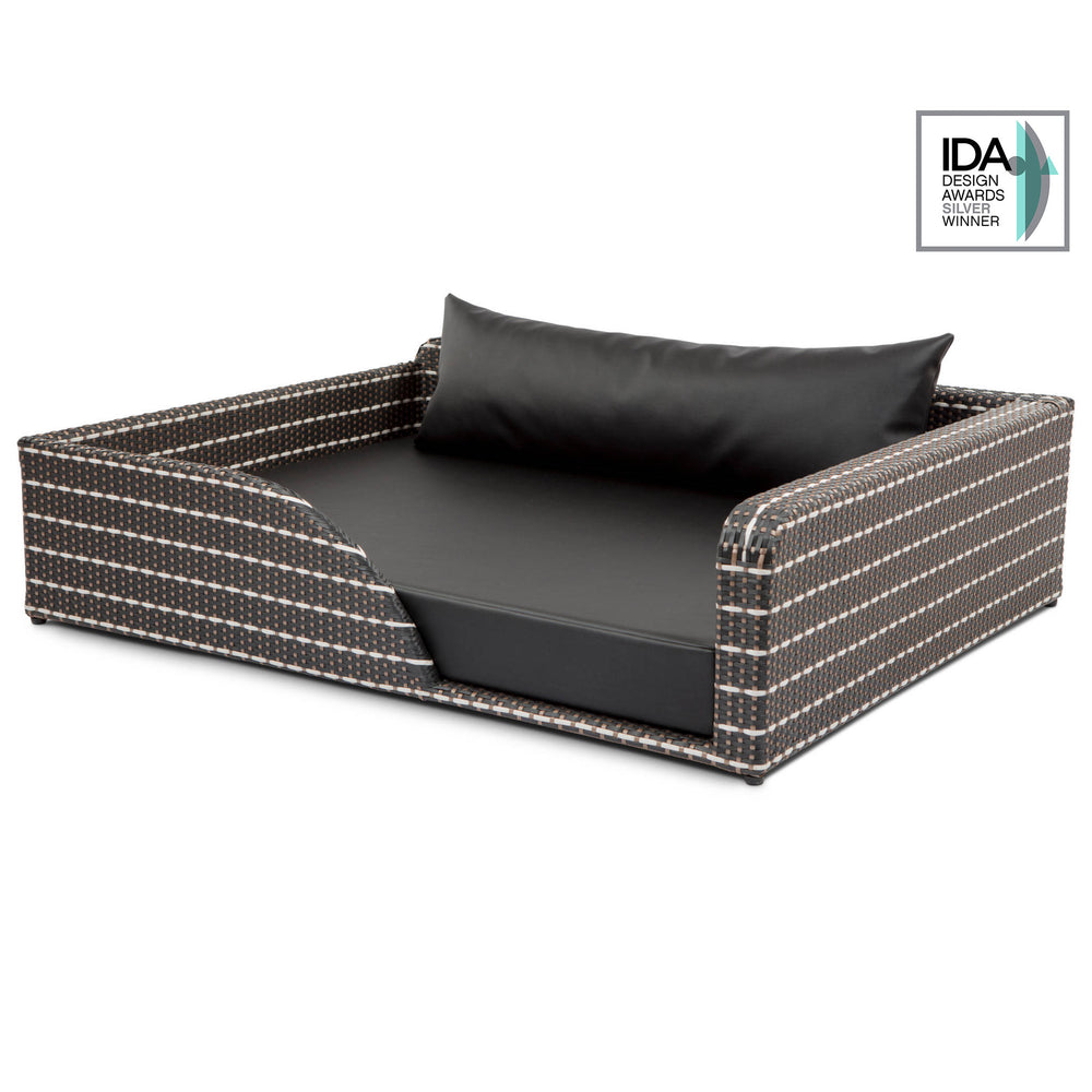 Elegantes Hundebett Cosmopolitan aus geflochtenem Material in dunklen Farben, rechteckig, mit schwarzem Kissen und Designpreis-Logo.