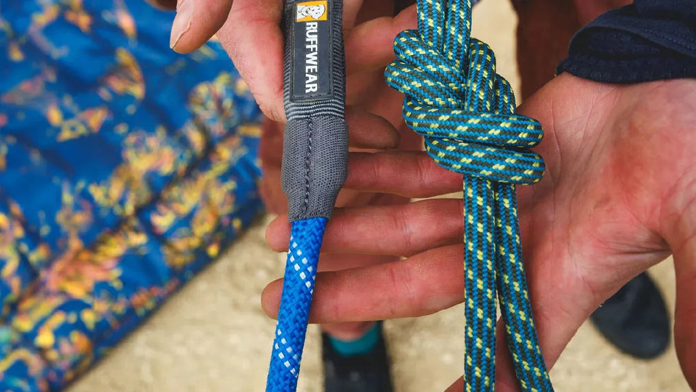 Hände arbeiten an einer blauen Kletterseil-Hundeleine mit grauer RUFFWEAR-Aufschrift, daneben ein grün-blaues Seil.