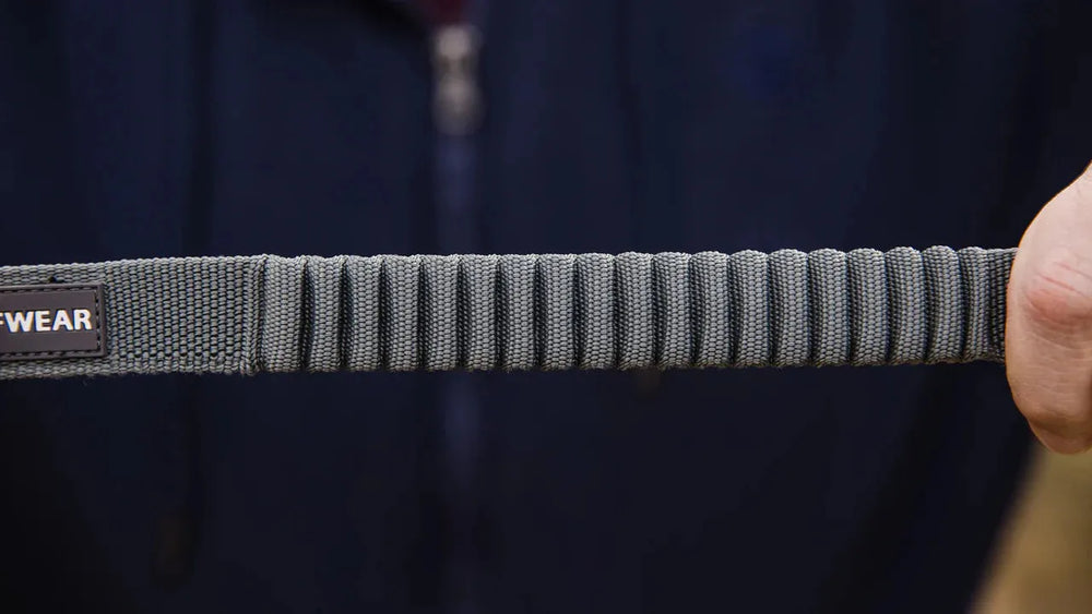 Graue Double Track™ Koppel für zwei Hunde, geflochten, elastisch und strapazierfähig, gehalten von einer Person.