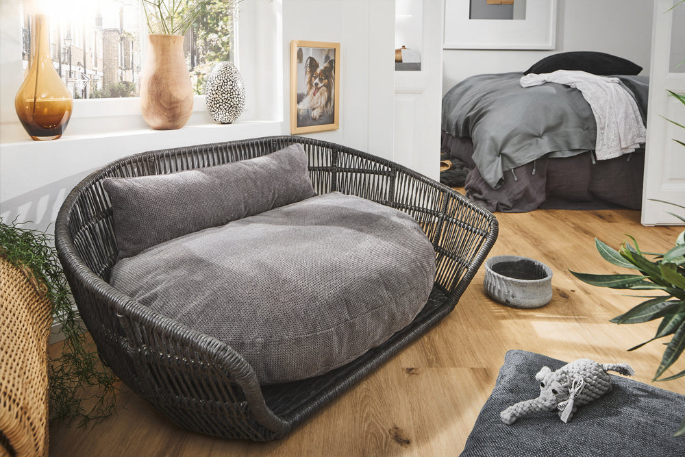Stilvolles Hundebett TUDOR in modernem Raum, rundes Design, geflochtenes Material, neutrale Grautöne, gemütliche Kissen.