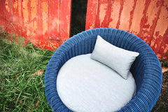 Hundebett Bellini: Blauer Korbsessel mit grauem Kissen auf Rasen, vor roten Holztüren. Ideal für Hunde.
