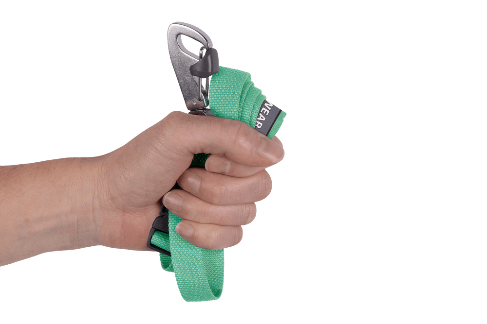 Hand hält eine grüne Flagline™ Hundeleine mit Metallkarabiner, Etikett „WEAR“ und strukturierter Oberfläche.