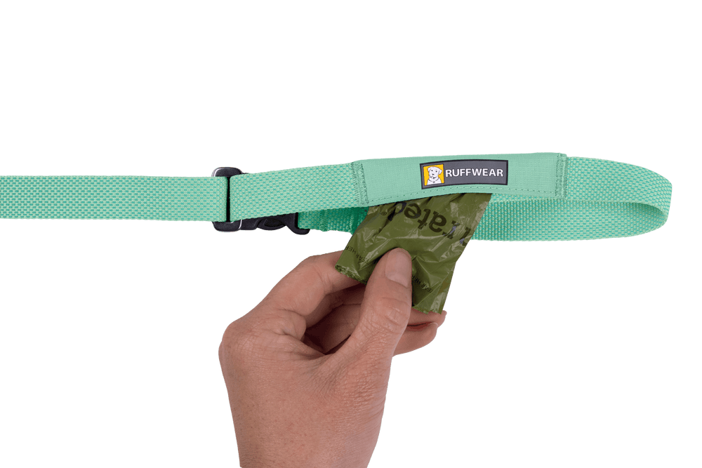 Mintgrünes Ruffwear Hundehalsband mit Futterhalter, in der Hand eine Tüte für Snacks oder Kotbeutel.