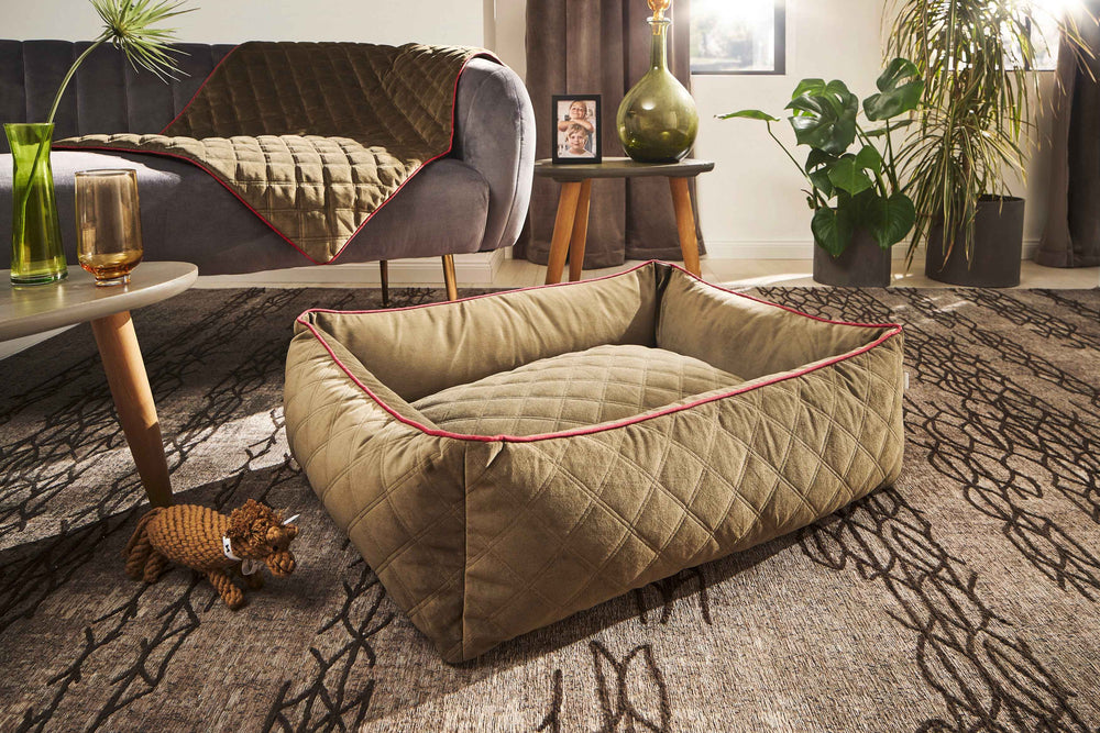 Beige-braunes CLASSIC Hundebett OXFORD mit roten Kanten im Wohnzimmer, umgeben von Sofa und dekorativem Tisch.