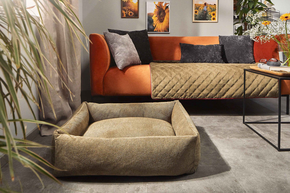 Beiges CLASSIC Hundebett TUDOR in modernem Wohnzimmer mit orangefarbenem Sofa und Sonnenblumenbildern.