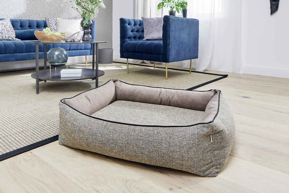 Elegantes ORTHO Hundebett SCALA in grau-beige im Wohnzimmer, stilvoll kombiniert mit Sofa und Sessel.