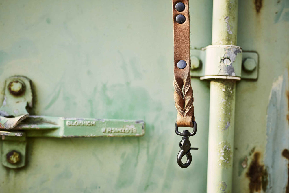 Braune Lederriemen-Leine mit Verzierung und schwarzem Karabinerhaken auf rostiger Metalloberfläche.