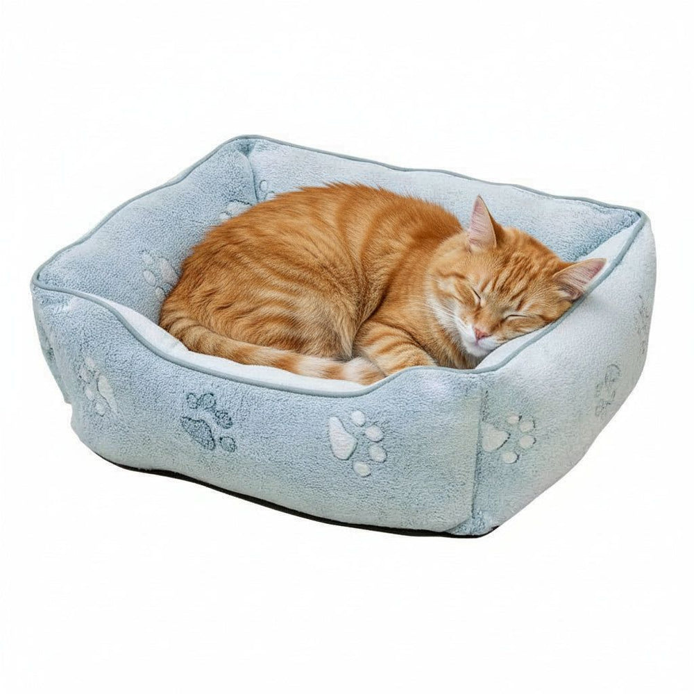 "Rechteckiges Kuschelbett 'PAW' für Katzen in Blau mit Pfotenabdrücken und schlafender oranger Katze."