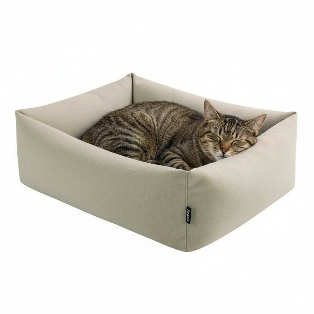 "Gemütliches rechteckiges Katzenbett 'NELU' in hellbeigem Stoff mit schlafender getigerter Katze."